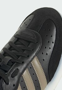 Czarne sportowe buty wykonane z materiału skórzanego i zamszowego, okrągły czubek, płaskie sznurowadła oraz trzy tonowe paski. Biała gumowa podeszwa i perforowane detale.