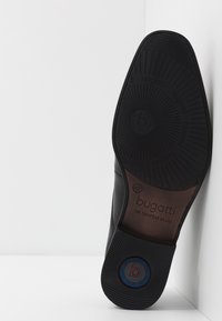 Semelle de chaussure en cuir noir avec une bande de roulement en caoutchouc texturé. Présente un logo embossé et le nom de la marque. Semelle intérieure marron visible avec indication de la taille.