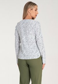 Biała koszula z długim rękawem z czarnym wzorem w stylu odręcznym, zestawiona z oliwkowymi spodniami, z zaokrąglonym dołem i miękkim materiałem.