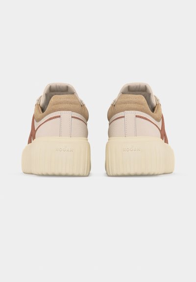 Ζεύγος μπεζ και καφετέ παπουτσιών με χοντρές ριμπεσμένες κρεμ σόλες, απεικονιζόμενα από πίσω, σε απλό ανοιχτό γκρι φόντο.