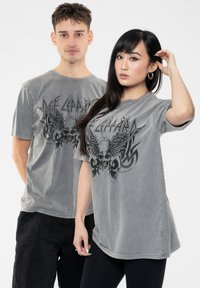 Gray cotton t-shirts with a faded finish, featuring a black graphic design of skulls and wings on the front. Short sleeves, relaxed fit.