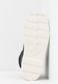 Scarpa con tomaia blu scuro, suola in gomma bianca texturizzata e dettagli del logo in rilievo. Taglia contrassegnata come 37. Orientamento del design verticale.