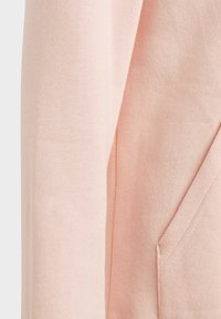 Felpa rosa chiaro con una consistenza morbida, maniche lunghe e tasca frontale. Il tessuto appare liscio con una leggera elasticità.