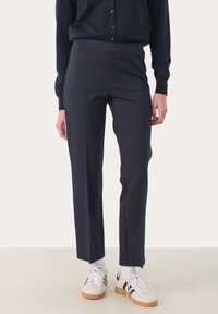 Pantalons ajustés bleu marine en tissu extensible, dotés d'une taille haute, de jambes droites et de coutures frontales discrètes. Associés à des baskets blanches.