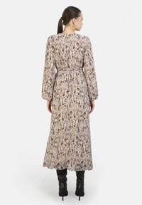 Vestido largo y estampado en beige con acentos en marrón y verde, que presenta mangas largas, una cintura ajustada y una falda fluida.