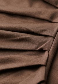 Brun tyg med en strukturerad yta, med veck som skapar mjuka veck. Mjuk, lätt och slät, perfekt för kläder.