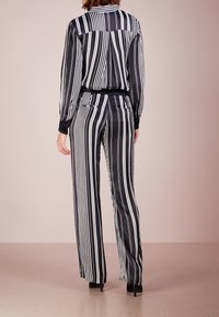Black and white striped blouse and pants set. Smooth, shiny fabric; long sleeves; fitted waist; loose-fitting trousers; high heels.