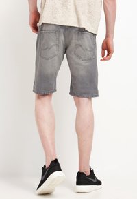 Shorts de mezclilla gris con un acabado desgastado, dos bolsillos traseros y detalles cosidos, combinados con zapatillas deportivas negras.