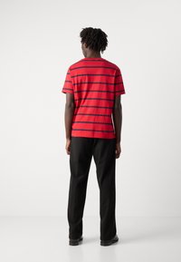 Rød kortærmet t-shirt med marineblå vandrette striber, lavet af bomuldsmateriale, afslappet pasform, parret med sorte bukser og sko.