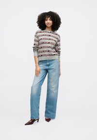 Grå tröja med röda och svarta "JOOP! JEANS"-mönster, kombinerad med ljusblå vida jeans. Modellen bär mörka högklackade skor.