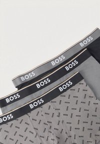 Three pairs of men's boxer briefs in black and two shades of gray, featuring elastic waistbands with white "BOSS" branding and a patterned design.