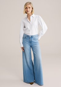 White button-up shirt with puff sleeves, paired with wide-leg light blue jeans. The jeans feature a high waist and classic five-pocket design.