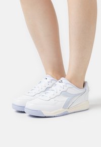 White sneakers with light blue accents, perforated leather, and textured sole. Laced design with padded collar for comfort.