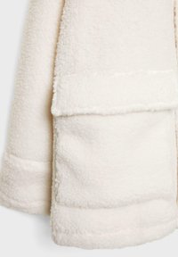 Veste en polaire blanche montrant une surface douce et texturée avec une poche à rabat pliée à l'avant et un design épuré et minimal.
