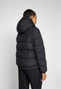 Veste doudoune noire avec capuche, présentant un design à cloisons, des poignets élastiques et un ourlet resserré. Le matériau semble lisse et durable.