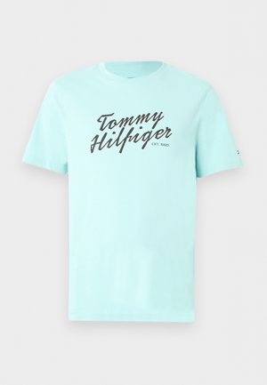 T-shirt bleu clair à manches courtes avec le texte noir en cursive "Tommy Hilfiger" et "EST. 1985" sur le devant, col rond côtelé.