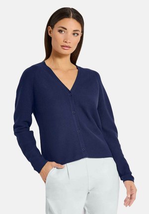 Marineblauer Cardigan aus weichem Strickstoff, mit V-Ausschnitt, langen Ärmeln und Knöpfen entlang der Vorderseite. Kombiniert mit hellen Hosen.