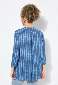 Blau gemusterte Bluse mit Dreiviertelärmeln, die ein vertikales Streifendesign und eine subtile Textur aufweist. Ausschnitt im Rücken, lockere Passform.