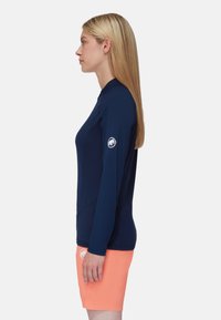 Navy Langarm-Rashguard mit hohem Kragen, tailliertem Design und Logo am Ärmel; kombiniert mit leuchtend korallenfarbenen Badeshorts.