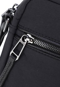 Sezione di borsa in nylon nero con una tracolla in pelle texture, una zip argentata e una corsia della zip liscia. Le maniglie si estendono per un facile trasporto.