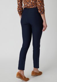 Pantaloni slim-fit blu navy con una texture liscia, dotati di una tasca posteriore e una vita media. Abbinati a ballerine in suede marrone.