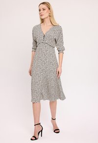 Czarna i biała midi sukienka w wzory, z dekoltem w kształcie litery V, długimi rękawami i dopasowaną talią, zestawiona z czarnymi, cienkimi szpilkami.