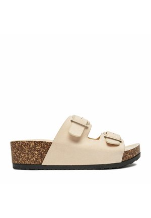 Beige Wildleder-Slidesandale mit zwei verstellbaren Schnallenriemen, Korkkeilsohle und schwarzer, strukturierter Gummilaufsohle, Seitenansicht.