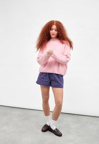 Rosa flauschiger Pullover, gestreifte marineblaue Shorts, weiße Socken und dunkle Slipper. Relaxed Fit, lange Ärmel und Rippdetails am Saum.