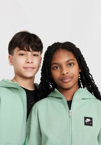 Mintgröna zip-up huvtröjor med framfickor och svart Nike Air-logotyp. En modell bär en svart skjorta under, som visar varumärket.