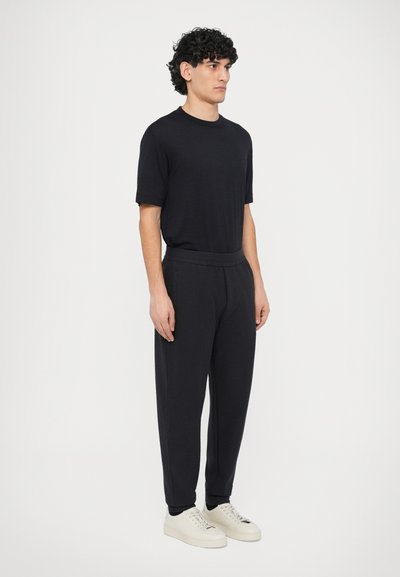 Czarny t-shirt z krótkim rękawem zestawiony z ciemnymi spodenkami typu jogger i białymi trampkami. Tkanina wydaje się miękka i teksturowana, o luźnym kroju.