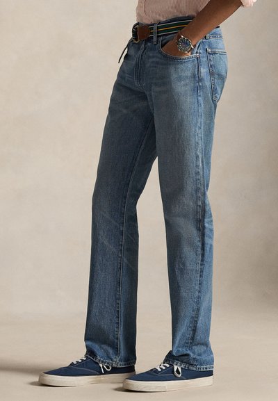 Ανοιχτό μπλε τζιν παντελόνι με ίσια γραμμή, διαθέτει θηλιές για ζώνη και μπροστινές τσέπες, σε συνδυασμό με ναυτικό μπλε αθλητικά παπούτσια.