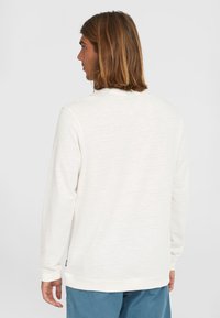Hvid langærmet sweatshirt med et struktureret mønster, rund halsudskæring og ribbede manchetter. Baggrunden er ensfarvet og lys.
