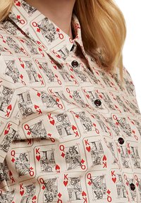 Button-up Hemd mit hellem Hintergrund und wiederholtem Muster von Spielkarten in Schwarz und Rot sowie schwarzen Knöpfen.