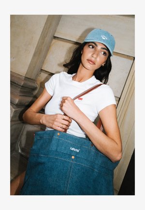 Λευκό T-shirt της Levi's με κόκκινο λογότυπο, τζιν τσάντα με μπλε ύφασμα, καφέ λουρί και ανοιχτό μπλε τζιν καπέλο. Απλή, casual σχεδίαση και χρώματα.