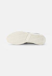 Semelle de chaussure avec une semelle extérieure en caoutchouc blanc texturé, présentant un motif en zigzag, conçu pour l'adhérence et la durabilité.