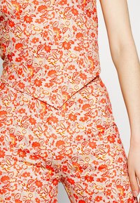 Combinaison florale avec une base rose et des fleurs rouges et jaunes. Tissu léger, décolleté en V et détails de taille cintrée.