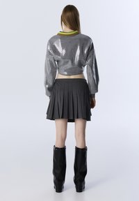 Cropped gray sequined sweater with long sleeves, paired with a pleated dark gray skirt and knee-high black heeled boots.