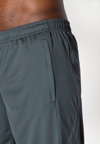 Os calções atléticos cinzentos apresentam um tecido texturizado, cintura elástica, bolso lateral e um corte descontraído, adequado para uso ativo.