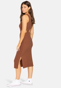 Braunes, geripptes Midikleid mit seitlichen Schlitzen und Cut-Out-Details. Kombiniert mit weißen High-Top-Sneakers. Glatte Textur und taillierte Silhouette.