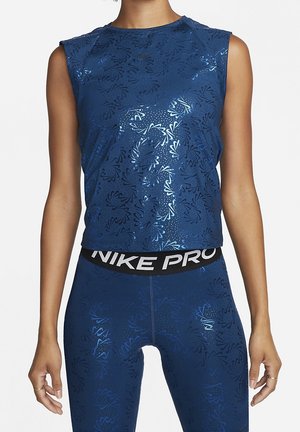 Vrouw draagt blauwe mouwloze sporttop en bijpassende legging met subtiel patroon en zwarte tailleband met label "NIKE PRO."