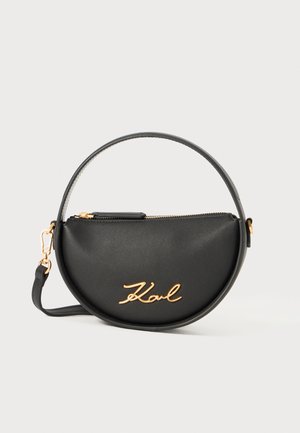 Black circular handbag made of smooth material with a gold zipper, featuring a gold script logo on the front and a top handle.