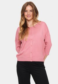 Light pink cardigan with three-quarter sleeves, round neck, and button closure. Soft texture with ribbed hem and cuffs. Black pants below.