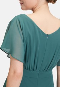 Teal Kleid mit fließenden, transparenten Schmetterlingsärmeln und V-Ausschnitt hinten. Verfügt über einen diskreten Reißverschluss am Rückenteil und eine geraffte Taille.