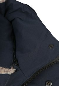 Vooraanzicht van het interieur van een marineblauwe jas met gladde stof, een ritssluiting, zwarte hardware en een nep-bonten rand langs de rand.