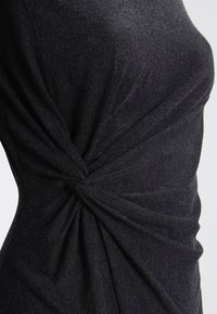 Schwarzes Oberteil aus Stoff mit einem verdrehten Designelement, das eine glatte Textur und eine figurschmeichelnde Silhouette zur Schau stellt, wobei der Stofffluss und die Drapierung betont werden.