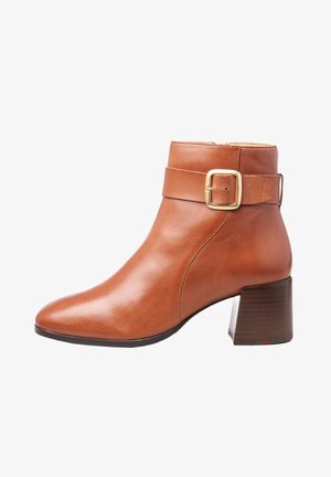 Bottine en cuir marron avec talon bloc et détail de bride à boucle dorée sur le côté, finition lisse, et fermeture éclair latérale.