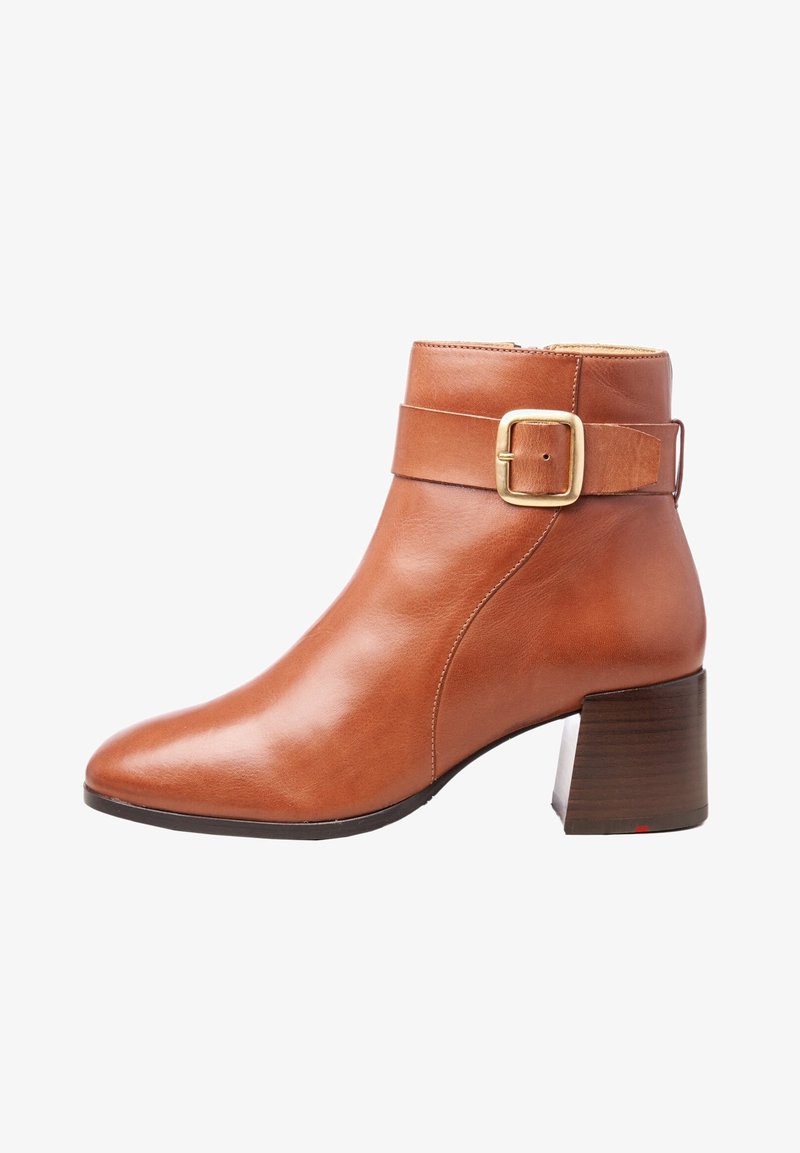 Bottine en cuir marron avec talon bloc et détail de bride à boucle dorée sur le côté, finition lisse, et fermeture éclair latérale.