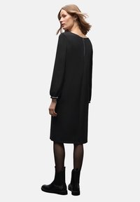Czarna sukienka z długim rękawem o okrągłym dekolcie, z tylnym suwakiem i dopasowanymi rękawami. Stylizowana z botkami za kostkę i przezroczystymi rajstopami.