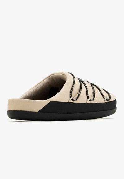 Chaussure beige sans lacets avec semelle noire et lacets décoratifs noir et blanc sur le dessus, vue de côté.