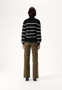 Pull rayé noir et blanc à col haut, associé à un pantalon en velours côtelé olive et des bottes noires à talons, vu de dos.